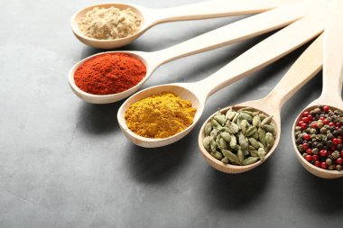 Gri masadaki kaşıklardaki farklı baharatlar, yakın plan.