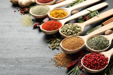 Siyah masada kaşıklardaki farklı aromatik baharatlar, yakın plan. Metin için boşluk