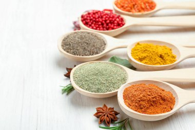 Beyaz ahşap masadaki kaşıklarda farklı aromatik baharatlar, yakın plan.
