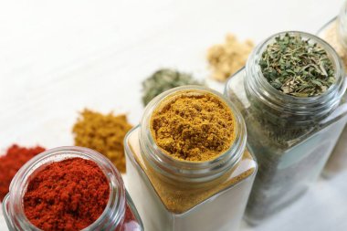 Beyaz masadaki kavanozlarda farklı aromatik baharatlar, yakın plan.