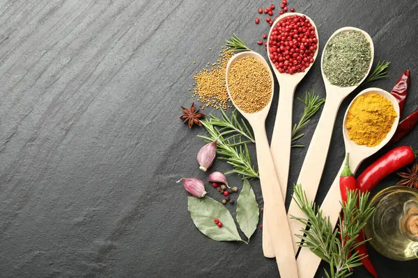 Siyah masadaki kaşıklardaki farklı aromatik baharatlar. Metin için boşluk