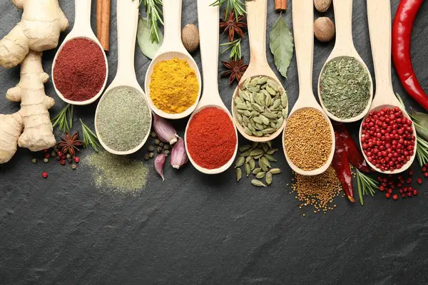 Siyah masadaki kaşıklardaki farklı aromatik baharatlar. Metin için boşluk