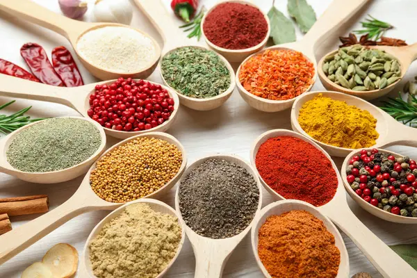 Beyaz ahşap masadaki kaşıklarda farklı aromatik baharatlar, yakın plan.