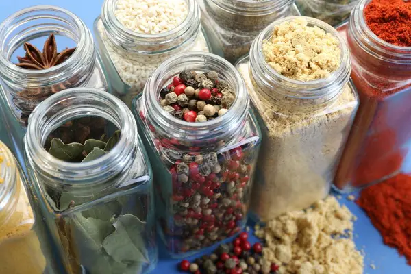 Mavi arka planda kavanozlardaki farklı aromatik baharatlar, yakın plan.