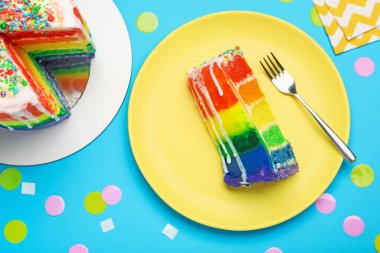 Açık mavi masada konfetiyle servis edilen nefis gökkuşağı pastası.