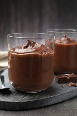 Lezzetli puding ve çikolata parçaları gri masada, yakın plan.