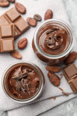 Cam kavanozlarda lezzetli puding, çikolata ve kakao çekirdekleri açık gri masada, düz yatıyordu.