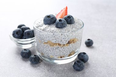 Chia tohumlu lezzetli puding, yoğurt, yaban mersini, granola ve çilek açık gri masada, yakın plan. Süper yemek.