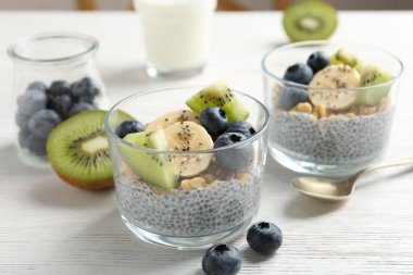 Chia tohumlu lezzetli tatlı, yoğurt, granola, yaban mersini, muz ve kivi beyaz ahşap masada, yakın plan. Süper yemek.