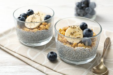 Chia tohumlu lezzetli tatlı, yoğurt, granola, yaban mersini ve muz beyaz ahşap masada, yakın plan. Süper yemek.