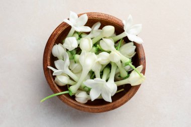 Üzerinde yasemin çiçekleri olan bir kase bej masa, üst manzara.