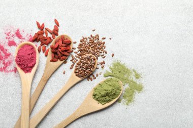 Açık gri masada, düz yerde, kaşıklarda farklı süper yiyecek tozları.