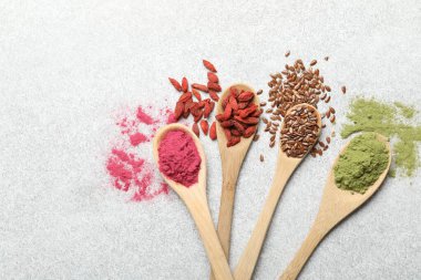 Açık gri masada, düz yerde, kaşıklarda farklı süper yiyecek tozları.