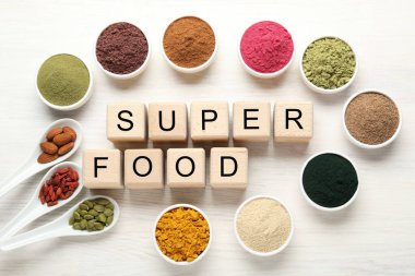 Farklı süper yiyecek tozları ve beyaz masadaki küplerden yapılmış kelimeler.