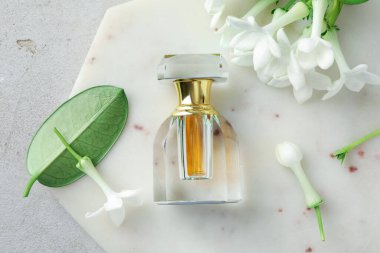 Parfüm ve yasemin çiçekleri açık gri masada, üst tarafta.