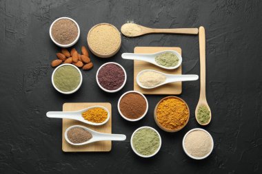 Farklı süper yiyecek tozları kaşık ve kâselerde koyu desenli masa, düz yatıyordu.