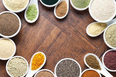 Tabaklardaki farklı süper yiyecek tozlarının çerçevesi ve tahta masa üzerindeki kaşıklar, düz yatış. Metin için boşluk