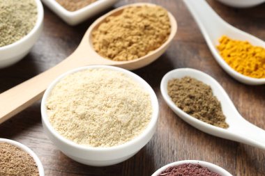 Tabaklardaki farklı süper yiyecek tozları ve tahta masada kaşıklar, yakın plan.