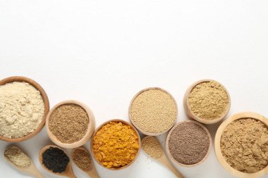 Kâselerde farklı süper yiyecek tozları ve beyaz arka planda kaşıklar, düz yatış. Metin için boşluk