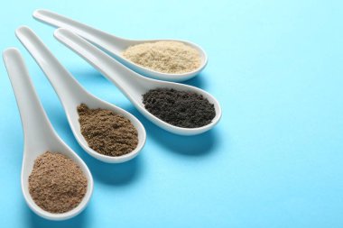 Açık mavi arka planda kaşıklarda farklı süper yiyecek tozları, yakın plan. Metin için boşluk