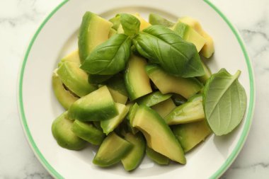 Beyaz mermer masada olgun yeşil avokado ve fesleğen kes.