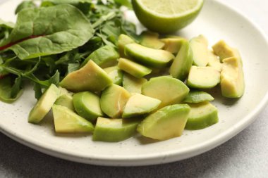 Olgun yeşil avokado, yeşil yeşiller ve açık gri masada limon, yakın plan.