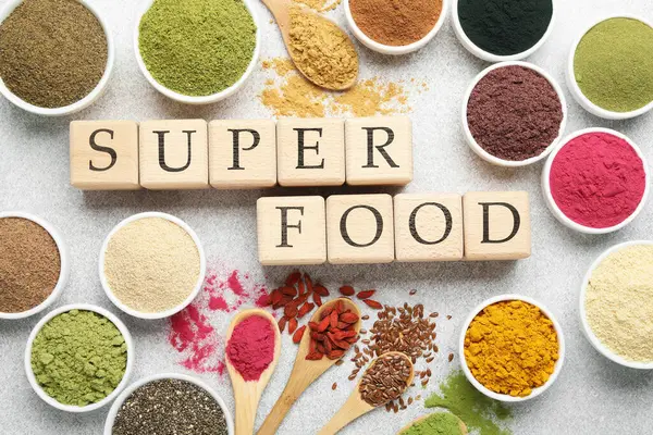 Farklı süper yiyecek tozları ve açık gri masadaki küplerden yapılmış kelimeler.