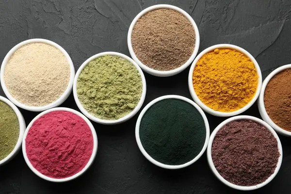 Koyu dokulu masada, düz bir zeminde, kaselerdeki farklı süper yiyecek tozları.