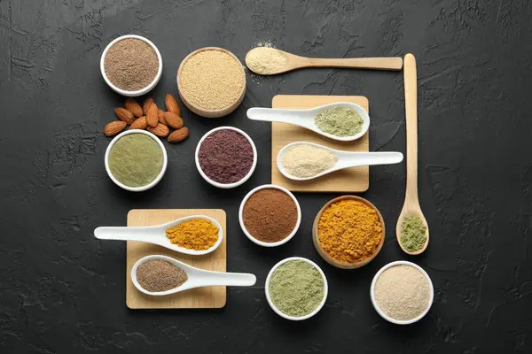 Farklı süper yiyecek tozları kaşık ve kâselerde koyu desenli masa, düz yatıyordu.