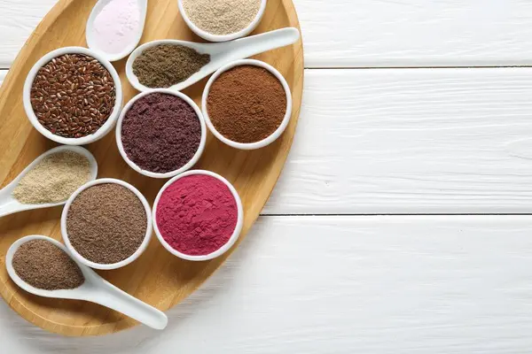 Kâselerdeki farklı süper yiyecekler ve beyaz ahşap masada kaşıklar, üst manzara. Metin için boşluk