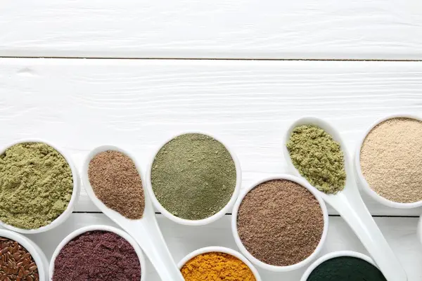 Kâselerdeki farklı süper yiyecek tozları ve beyaz ahşap masa üzerindeki kaşıklar düz yatıyordu. Metin için boşluk