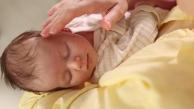 Anne yeni doğmuş bebeğini evde okşuyor, yakın plan.