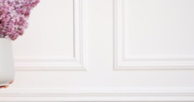 Evdeki beyaz duvarın yanında güzel leylak çiçekleri düzenleyen bir kadın.