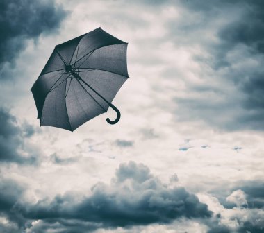 Bulutlu gökyüzünde uçan siyah şemsiye. Fırtınalı hava