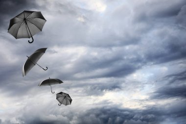 Bulutlu gökyüzünde uçan siyah şemsiyeler. Fırtınalı hava