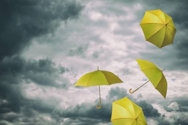 Bulutlu gökyüzünde uçan sarı şemsiyeler. Fırtınalı hava