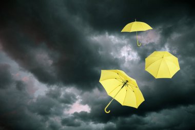 Koyu bulutlu gökyüzünde uçan sarı şemsiyeler. Fırtınalı hava
