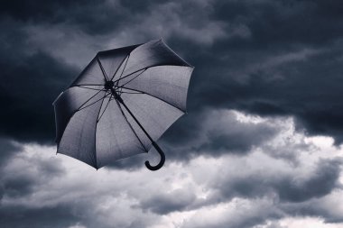 Kara bulutlu gökyüzünde uçan siyah şemsiye. Fırtınalı hava