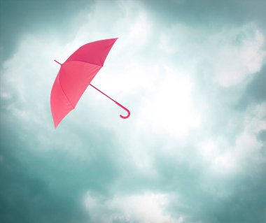 Bulutlu gökyüzünde uçuşan pembe şemsiye. Fırtınalı hava