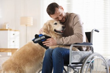 Tekerlekli sandalyedeki adam evde hizmet köpeğine sarılıyor.