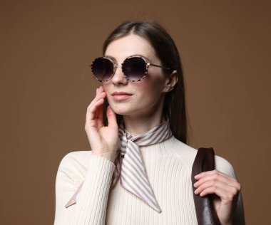 Kahverengi arka planda şık giyinmiş güzel bir kadının moda portresi.