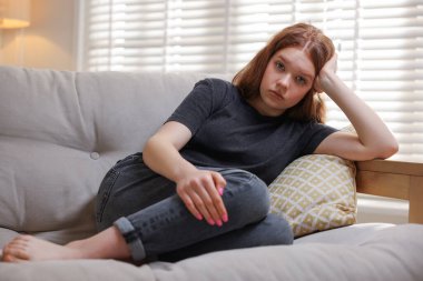 Evdeki kanepede oturan üzgün genç kız.