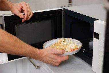 Yemek tabağını mikrodalgaya koyan adam, yakın plan.