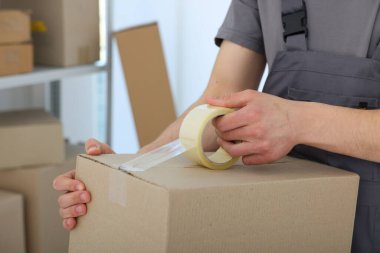 Kapalı alanda yapıştırıcı bantlı karton kutu mühürleyen adam.