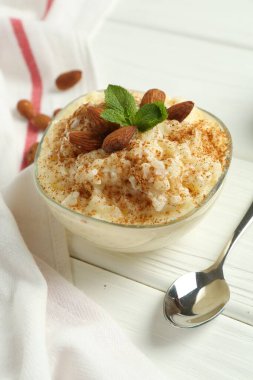 Tarçınlı lezzetli pirinç pudingi, beyaz ahşap masada nane ve badem, yakın plan.
