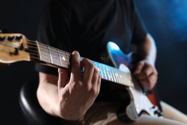Karanlık arka planda gitar çalan adam dumanlı, eline odaklan