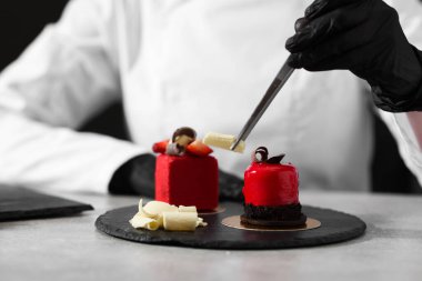 Mutfaktaki açık gri masada lezzetli bir tatlıyı dekore eden şekerci, yakın plan.