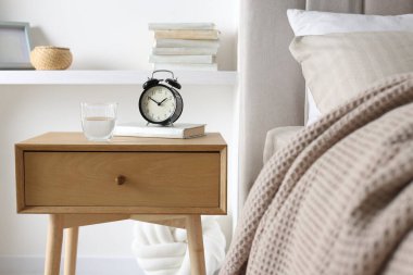 Alarmlı komodinli komodin, bir bardak su ve yatağın yanında kitap.