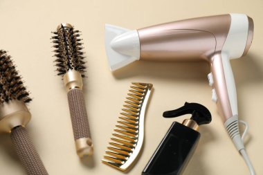 Bej arka planda yuvarlak fırçalar, sprey, tarak ve kurutucu, üst görünümde.