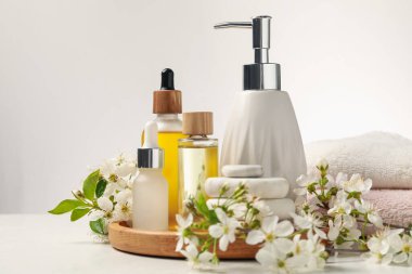 Spa ürünleri, çakıl taşları ve beyaz masadaki güzel çiçekli dallar, yakın plan.